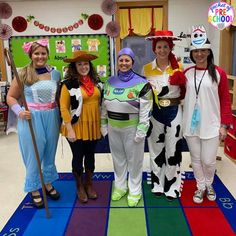 four women in costumes standing on a rainbow colored rug with one woman dressed as toy story book characters