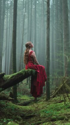 a woman in a red dress is sitting on a log in the middle of a forest