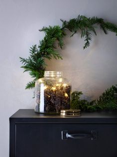 a black dresser topped with a glass jar filled with christmas lights and pine branches on top of it