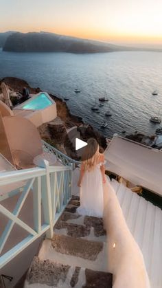 a woman in a wedding dress walking up some stairs to the water at sunset or sunrise