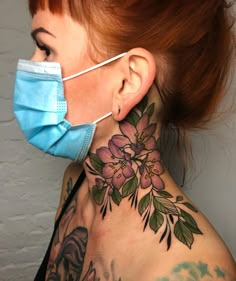 a woman wearing a face mask with flowers on her neck and behind her is a tattoo