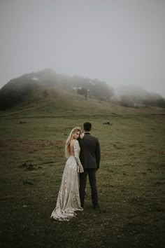 a bride and groom standing in a field with foggy hills behind them at their wedding