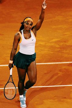 a woman holding a tennis racquet on top of a tennis court with her hand in the air