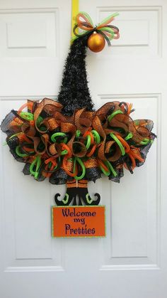 a welcome wreath hanging on the front door with an orange and green bow attached to it