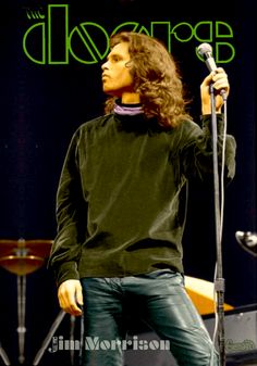 a man with long hair standing in front of a microphone and singing into a mic