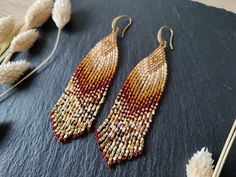 two pairs of beaded earrings sitting on top of a black surface next to dried flowers