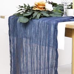 a blue table runner with flowers and greenery on the top, sitting next to a chair