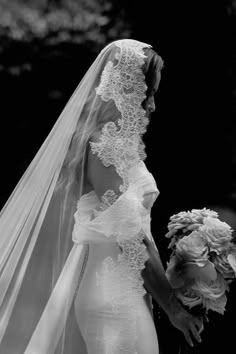 a woman in a wedding dress and veil walking with her flower bouquet to the groom