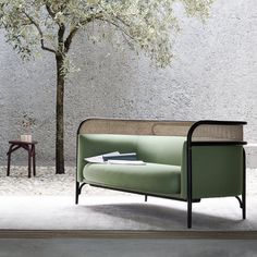 a green couch sitting under a tree next to a table with a book on it