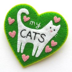 a green heart shaped brooch with a white cat and pink hearts on it's side