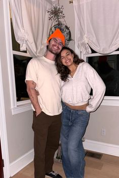 a man and woman standing next to each other in front of a window with curtains