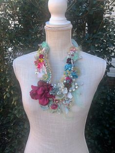 a white mannequin holding a multi colored necklace on it's neck with flowers