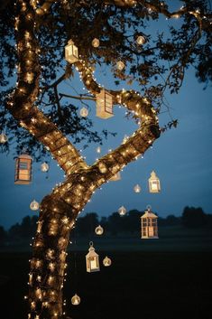 a tree with lanterns hanging from it's branches in the night sky, lit up by fairy lights