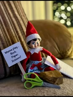 an elf is sitting on the floor next to a sign that says wanna't play rock paper scissors?