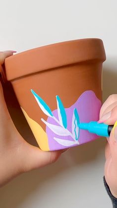 someone is painting a flower pot with blue and yellow paint on the outside of it