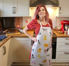 a woman standing in a kitchen wearing an apron with dogs on it and smiling at the camera