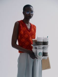 a woman holding a stack of coffee cups in her hand and wearing sunglasses on top of it