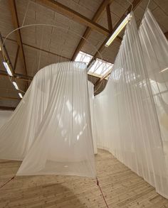 an empty room with sheer curtains hanging from the ceiling and wood flooring in front of it