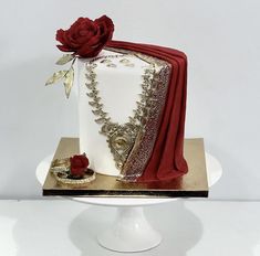 a white and red wedding cake on a gold plate with a rose in the middle