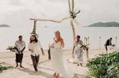 a bride and groom walk down the beach with their guests behind them as they exit the ceremony