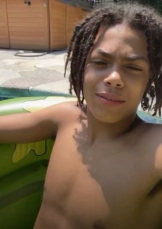 a shirtless boy with dreadlocks sitting in a pool