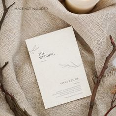 the wedding program is sitting on top of a table cloth next to some branches and a candle