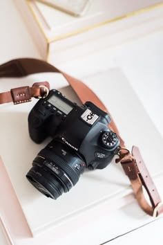 a camera sitting on top of a white box next to a brown leather belt and strap