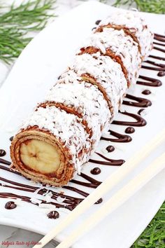 a white plate topped with chocolate and banana roll next to two chopsticks on top of it