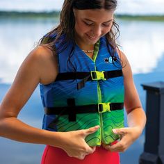 a woman standing next to a body of water holding her cell phone in her hands