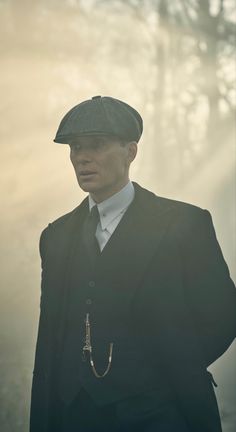 a man in a suit and hat standing next to trees with fog on the ground