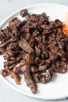 a white plate topped with meat and carrots on top of a gray countertop