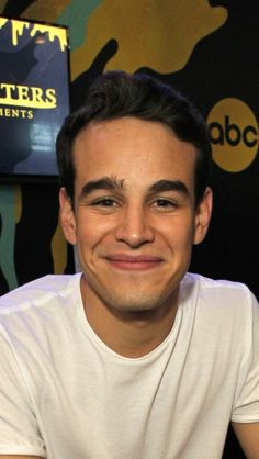 a young man smiling at the camera in front of a wall with letters on it