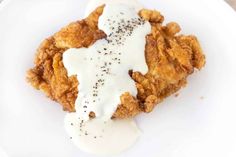 a white plate topped with fried chicken covered in ranch dressing