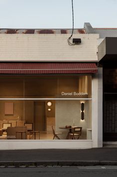 an empty storefront with chairs and tables in the window at dusk, on a city street