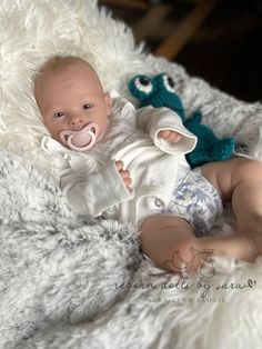 a baby laying on top of a white blanket next to an owl stuffed animal wearing a pacifier