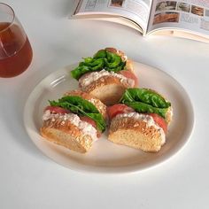 three sandwiches are on a plate next to a glass of tea and an open book