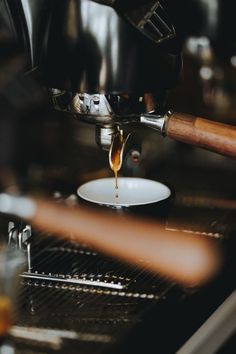 coffee being poured into a white bowl on top of a stove with an espresso machine in the background