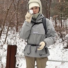 a woman is standing in the snow holding a cell phone to her ear and wearing gloves