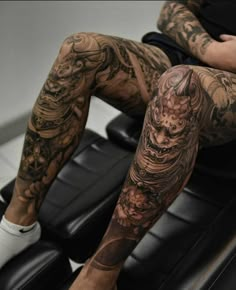 a tattooed man sitting in a chair with his legs crossed