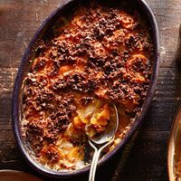 a casserole dish with potatoes and meat in it on a wooden table next to a spoon