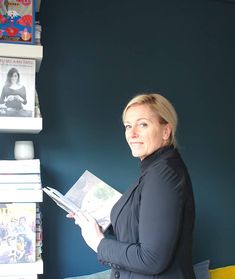 a woman standing in front of a stack of books and holding a book with her right hand