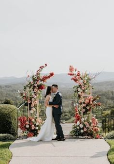 a bride and groom kissing in front of an outdoor ceremony arch with flowers on it