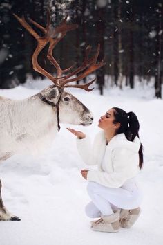 a woman kneeling down next to a reindeer in the snow