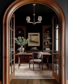 an archway leading into a home office with wood paneling and glass doors that lead to the dining room