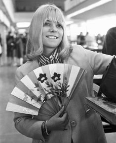 a woman is holding a fan and smiling at the camera while standing in an airport