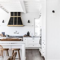 a kitchen with white cabinets and counter tops, an island in the middle is surrounded by wooden stools