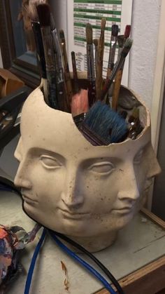 a ceramic head with paintbrushes and brushes in it on top of a table