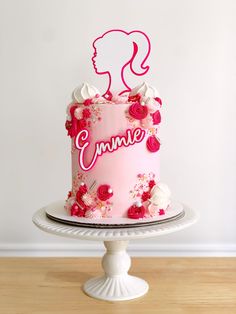 a pink cake decorated with flowers and the word emmett on top is sitting on a white pedestal