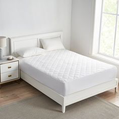 a white bed sitting next to a window in a bedroom on top of a wooden floor