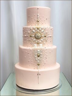 a three tiered wedding cake with pearls and jewels on the top, sitting on a glass table